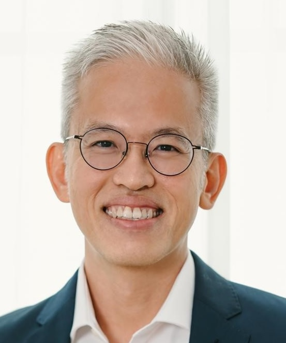 Smiling man with graying hair, wearing glasses and a dark suit.